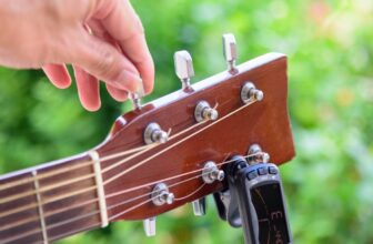 Guitariste en train d'accorder sa guitare acoustique à l'aide de la méthode des cinq frettes.