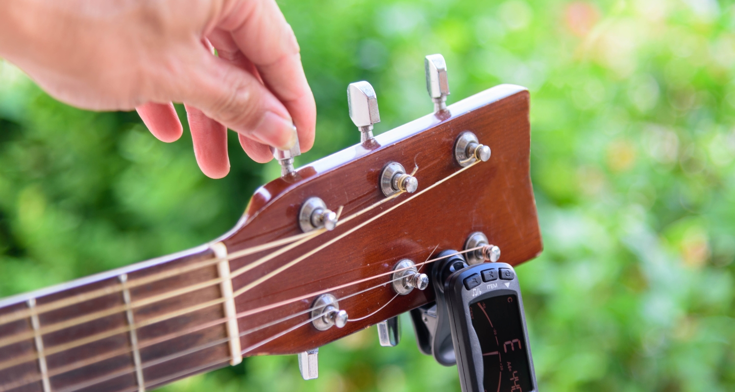 Guitariste en train d'accorder sa guitare acoustique à l'aide de la méthode des cinq frettes.